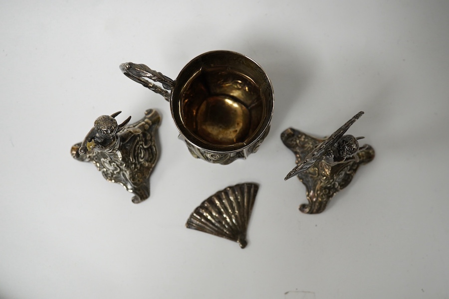 A small Victorian silver christening mug with embossed decoration and scroll handle, Hilliard & Thomason, Birmingham, 1860, 82mm and a pair of cast silver cherub figures holding fan, (Chester import marks) on triangular